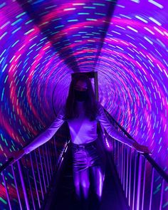 a woman in white shirt and purple pants walking down a tunnel with colorful lights on it