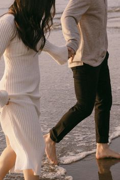 a man and woman holding hands walking along the beach with their feet in the water