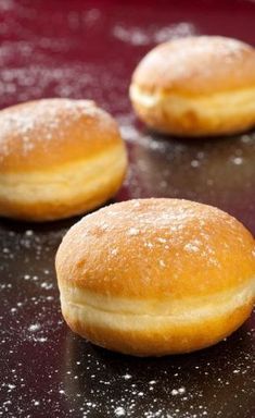 three donuts sitting on top of a table covered in powdered sugar