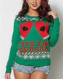 a woman wearing a green christmas sweater with an ugly red heart on the chest and words that read, it's the season