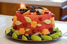 a colorful cake with fruit on it sitting on top of a white tablecloth covered plate