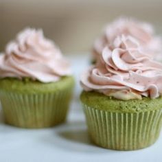 two green cupcakes with pink frosting sitting on a white cake platter