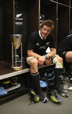 two rugby players sitting next to each other in the locker room with trophies and drinks