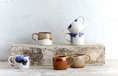 four coffee mugs sitting on top of a wooden shelf next to each other in front of a white wall