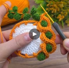 someone is crocheting an orange and white object with green leaves on it,