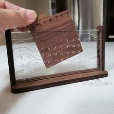 a person holding a small wooden calendar in front of a glass case on a table