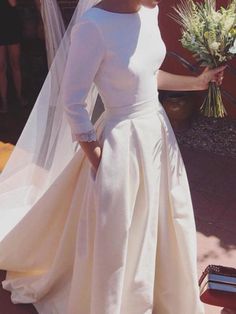 a woman in a white dress and veil is walking down the street with her bouquet