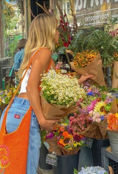 a woman standing in front of a flower shop with lots of flowers on the counter