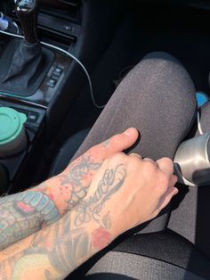 a person driving a car with tattoos on their arm and hand holding the steering wheel