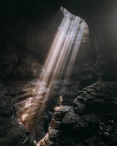 a person standing in the middle of a cave with sunlight coming from behind it and on top of some rocks