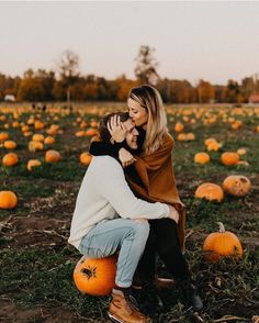 two people sitting on top of pumpkins in a field with one holding the other