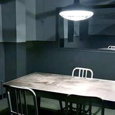 a table and chairs in a room with black walls, white ceiling lights and grey flooring