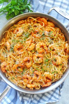 pasta with shrimp and parsley in a pan on a blue checkered table cloth