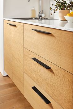 a kitchen with wooden cabinets and white counter tops, has black handles on the drawers