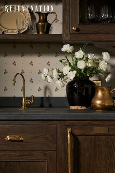 a vase with white flowers sitting on top of a kitchen counter next to a gold faucet