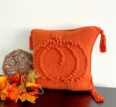 an orange crocheted pillow sitting on top of a wooden table next to flowers