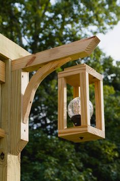 a bird feeder hanging from the side of a wooden structure with trees in the background