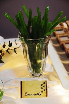 there is a glass vase with some green plants in it and cookies on the table