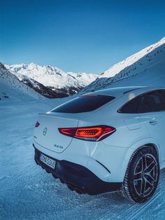 the rear end of a white mercedes suv parked on snow covered ground with mountains in the background