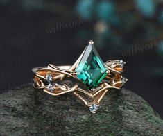 a gold ring with an emerald colored stone surrounded by diamonds on top of a rock