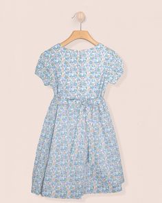 Demoiselle's Beauty Lies in Her Understated Elegance. Designed in a beautiful liberty floral print, this dress features a gathered smocked bodice along the chest for a more casual look. It is fully lined with short puff sleeves and matching self-tie sash with elegant buttons for a sophisticated touch. 100% Liberty of London Cotton. Fully Lined in Cotton. Delicate Machine Wash Cold, Flat Dry, Cool Iron, Dry Clean Fitted Cotton Smocked Dress With Ditsy Floral Print, Blue Dress For Garden Party With Gathered Neckline, Blue Cotton Dress With Gathered Waist, Blue Smocked Dress For Garden Party, Blue Floral Print Cotton Smocked Dress, Liberty Floral, Liberty Of London, Understated Elegance, Blue Dress