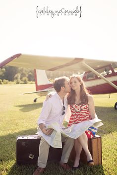 a man and woman sitting on suitcases kissing in front of an airplane