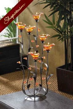 a metal candle holder with many lit candles in it on a table next to a potted plant