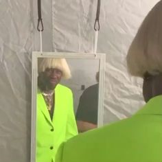 a woman in a lime green jacket is looking at herself in the mirror and smiling