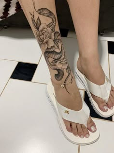 a woman's foot with a snake and flower tattoo on it, while she is wearing white sandals