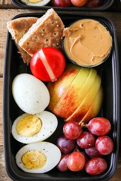 two black trays filled with different types of food on top of a wooden table