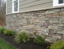 a stone wall in front of a house with grass and flowers growing next to it