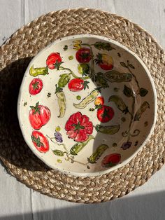 a bowl with tomatoes and peppers painted on it sitting next to a straw hat that is laying on the ground