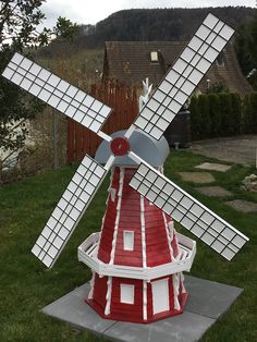 a red and white windmill sitting on top of a cement slab next to a green field