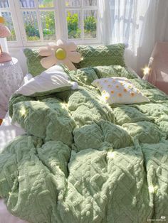 a bed with green comforter and pillows in front of a large flower on the headboard