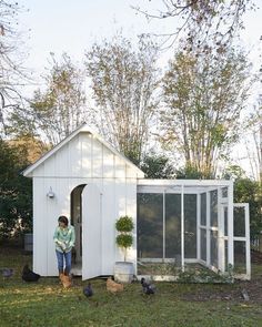 a woman standing in the doorway of a chicken coop with chickens around her and other birds nearby