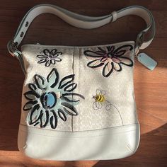 This Coach Floral Bee Can Work As A Hobo, Crossbody And Shoulder Bag. The Colors Are Great, Cream Leather And Canvas Signature Print, With Flowers In Pink, Blue And Gray/Purple, And Of Course One Bee In Yellow And Black. The Top Of The Bag Is Bordered With Beige Leather, As Well As The Bottom And The Strap. The Canvas Shows The Signature Print With Stitched Suede Flowers And The Fabric Bee With Rhinestone Head. The Strap Adjusts From 14" Perfect For Shoulder And Finally To 20" Crossbody. It Has A Keyfob And Tab On The Zip Closure. There Is One Nice Size Zipped Pocket In The Back Outside Perhaps For Phone Or Keys. There Are 3 Pockets Inside: Large Zip Closure, Phone Pocket And Smaller Pocket Beige Shoulder Bag With Embroidered Logo For Everyday Use, White Rectangular Shoulder Bag With Embroidered Logo, Everyday Leather Shoulder Bag With Embroidered Logo, Leather Shoulder Bag With Embroidered Logo For Everyday Use, White Tote Shoulder Bag With Embroidered Logo, Everyday White Embroidered Shoulder Bag, White Embroidered Shoulder Bag For Everyday, White Travel Bags With Floral Embroidery, White Embroidered Satchel Shoulder Bag