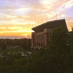 the sun is setting over a building and trees