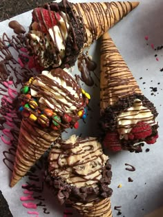 four ice cream cones covered in chocolate and sprinkles on top of a piece of paper