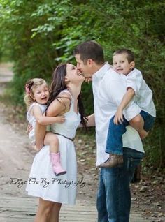 a man and woman kissing their children while standing on a wooden walkway in the woods