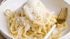 a white bowl filled with pasta covered in parmesan cheese next to a fork