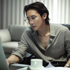 a man sitting in front of a laptop computer on top of a desk next to a cup