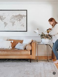 a woman standing next to a couch in a living room with a map on the wall