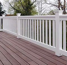 a wooden deck with white railings and trees in the backgroung area