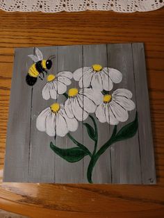 a painting of white daisies and a bee on a wooden board with lace doily