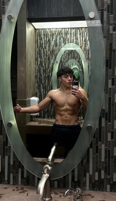 a shirtless man taking a selfie in the bathroom mirror with his cell phone