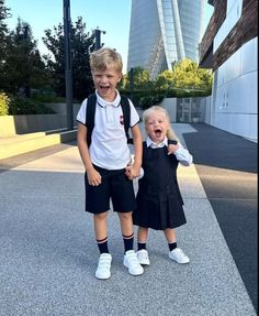 two young children standing next to each other in front of a building with tall buildings