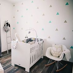 a baby's room decorated in white and green with triangles on the wall, crib, rocking chair, and bed