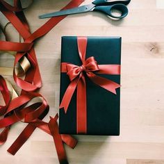 a gift wrapped in black and red ribbon next to scissors on top of a wooden table