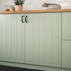 a kitchen with green cupboards and wooden counter tops on the wall, along with a potted plant