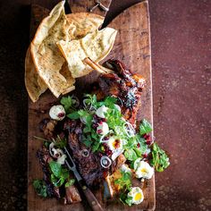 a wooden cutting board topped with meat and veggies next to tortilla chips